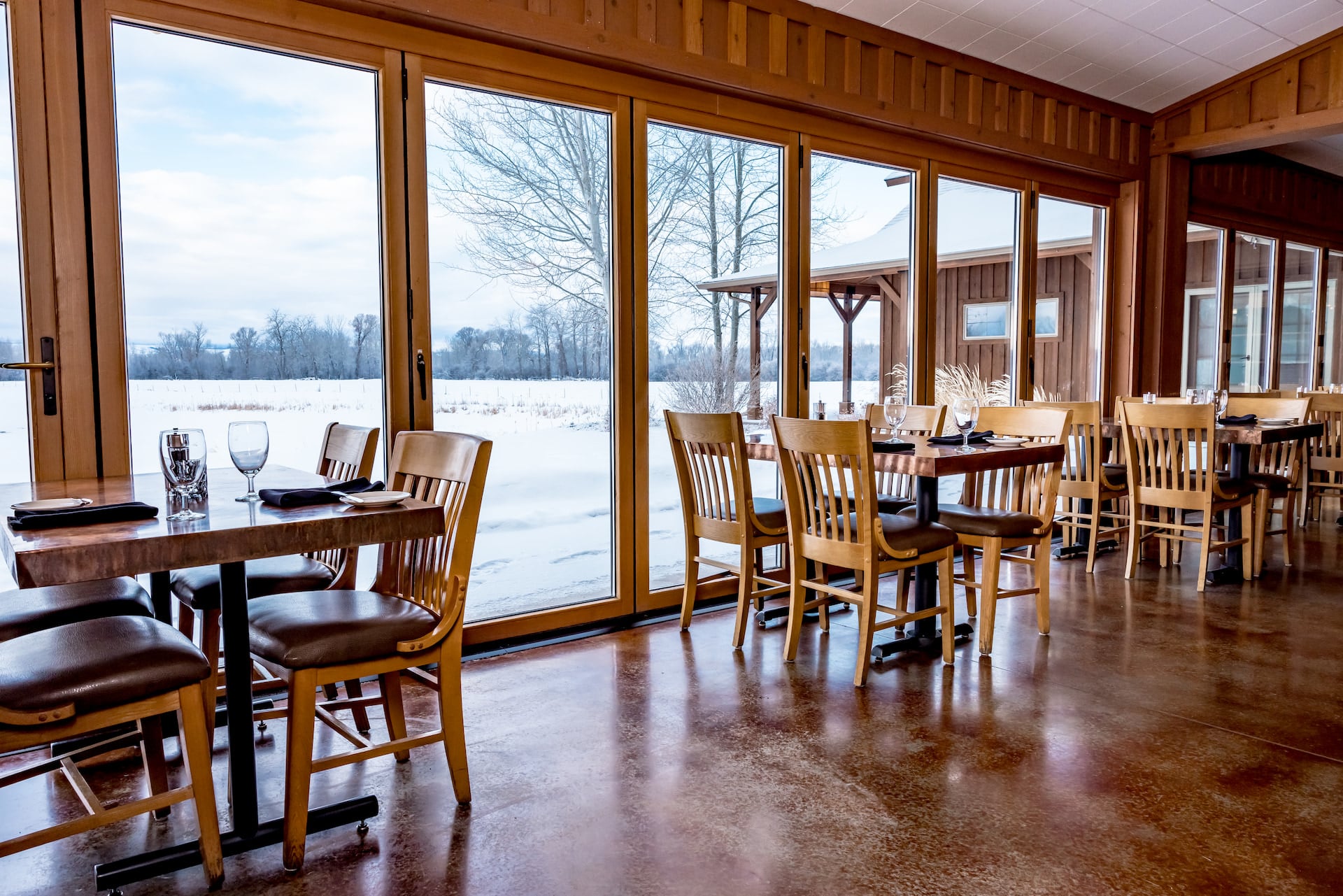 Cozy restaurant with snowy outdoor view through windows.
